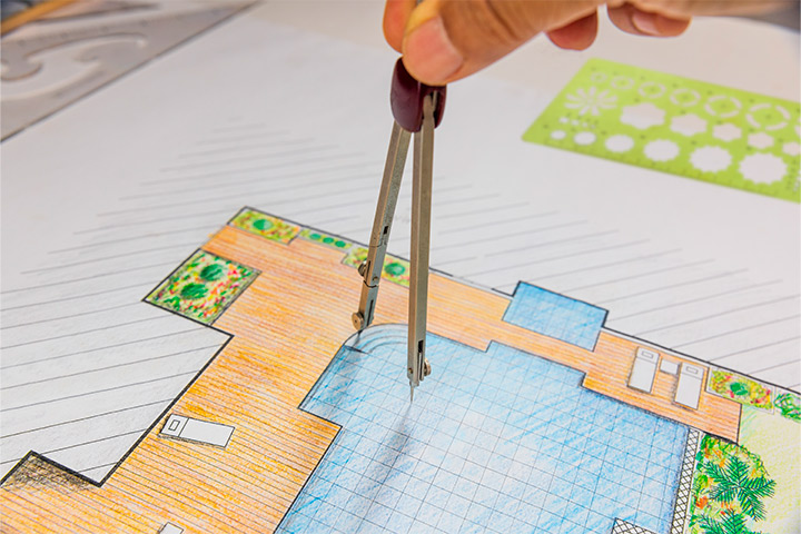 An individual holding scissors and drawing a house, representing the design process when hiring a pool builder in Houston.
