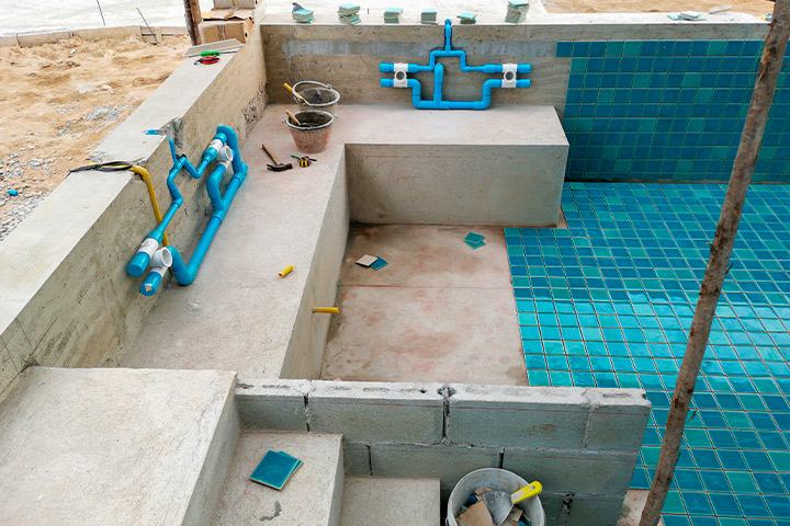 An image of a pool under construction, featuring blue pipes and cement, illustrating the pool building process in Houston.