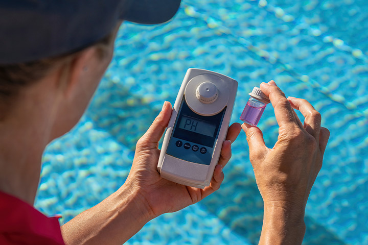 A pool technician checks the temperature with a digital thermometer near a swimming pool, assessing for potential repair needs.